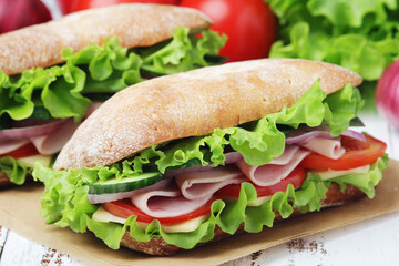Two sandwiches with fresh vegetables, ham and cheese in ciabatta bread