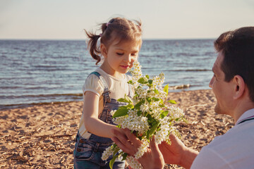 little girl runs to dad with bouquet of flowers on sunny day beach in summer