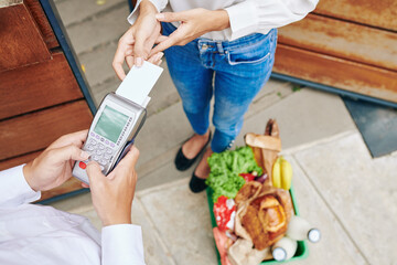 Horizontal from above shot of unrecognizable young woman paying for fresh food delivery service with her debit card