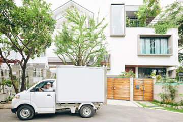 Horizontal long shot of modern Asian delivery man wearing white clothes driving van on sunny day,...