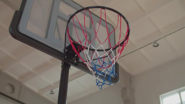Close-up of basketball going through basketball hoop on indoor court. African american basketball player scoring field goal with bank shot, ball bouncing off backboard and falling into hoop.