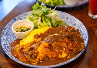 Hayashi rice (Hashed beef rice) on an omelette that is filled with fried rice (Omu Hayashi), salad and pickles in a Japanese restaurant