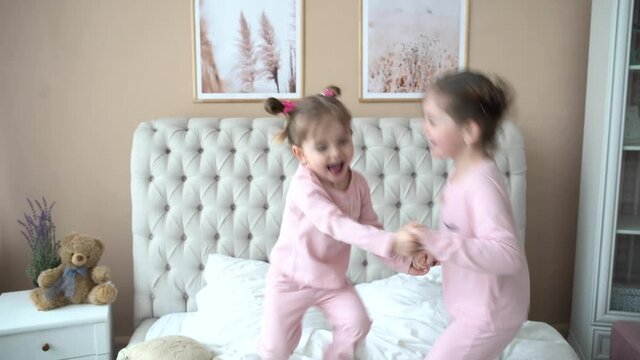 Portrait of children jumping on a bed, little girls, two sisters have fun and laughing, happy kids on quarantine, coronavirus home isolation