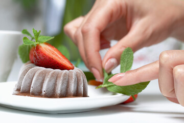 Chocolate fudge garnished with half a strawberry with petals. Woman decorates dessert with mint and...