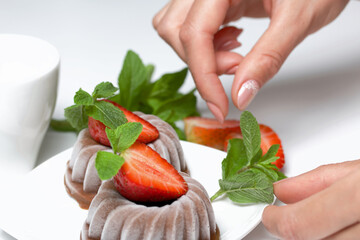 Chocolate fudge garnished with half a strawberry with petals. Woman decorates dessert with mint and...