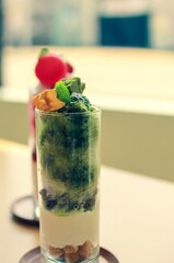 Green tea (Matcha) flavoured parfait with Japanese shaved ice (Kakigoori), cream, cookies. Warabi Mochi on top, another parfait in the background, on a table. Perfect dessert for summer.