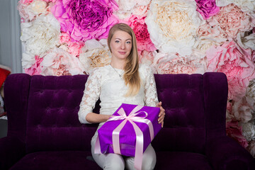 beautiful young blond woman looks at camera holding in hands big purple gift box