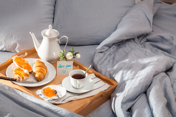 Breakfast in bed, a tray of tea, french croissants, jam. Love note. Honeymoon.  Sunnny morning at the hotel. In the process of eating.