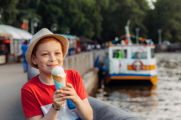 A redhead boy is eating ice cream at the pier. Children's walk