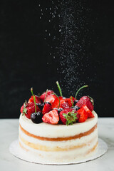 Open white cake with strawberries and cherries on a white background on a dark background. Powdered sugar powder. Fruit dessert.