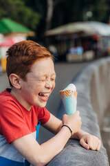A freckled redhead boy is eating ice cream and laughing at the pier. Children's walk
