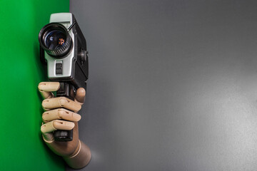 A wooden hand holds a vintage camera against a background of gray background. Video production. Selfy.