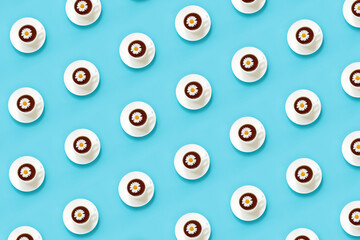 Pattern made from white cup of tea with chamomile on dish saucer, blue background. Top view Flat lay