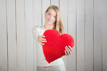 beautiful young blonde woman looks at camera showing red heart shaped pillow
