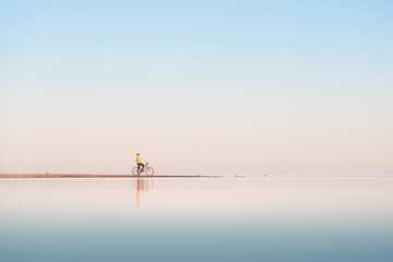 Cyclist on the shore of the calm sea. Distant plan.