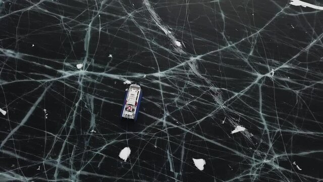 Aerial view of sliding hovercraft on frozen beautiful Baikal lake. Clip. Top view of the reservoir surface bound by thick cracked ice and a moving hovercraft.