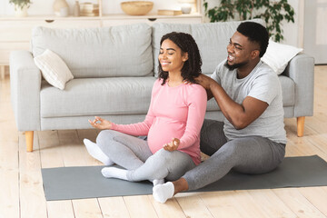 Fototapeta premium Attentive husband massaging his meditating pregnant wife
