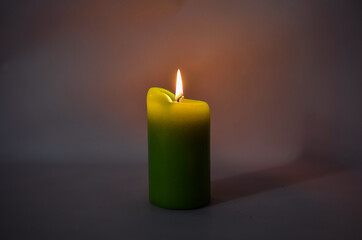 Big green candle on a dark background. The burning candle is yellow-green.