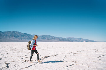 Woman wanderlust having active trip on vacation exploring death valley, hipster girl with backpack walking on dry arid surface of Badwater basin enjoying beautiful wild nature in american journey.