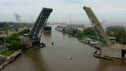 Aerial tracking shot of cargo ship navigating the Black River in Lorain Ohio to pass under open lift bridge on a foggy afternoon