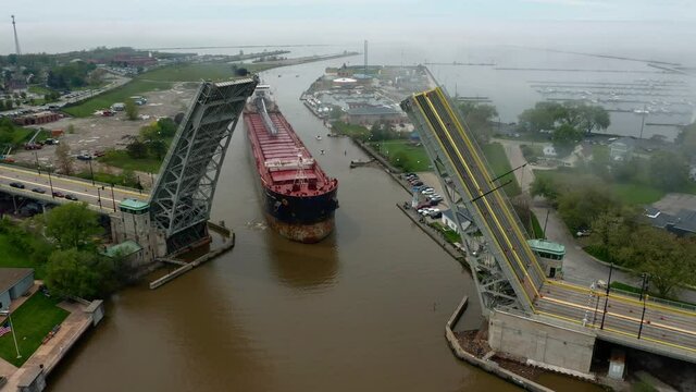 Aerial tracking shot of cargo ship navigating the Black River in Lorain Ohio to pass under open lift bridge (fog coming off of Lake Erie in background)