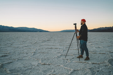 Professional male photographer using tripod for shooting video of sunset in death valley working at...