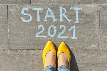 Start 2021 year concept, top view on woman legs and text written in chalk on gray sidewalk