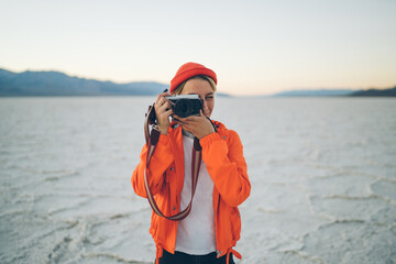 Skilled blonde woman traveler holding camera with modern objective taking photos of nature...