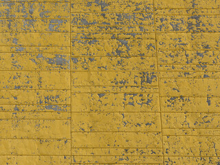 Weathered and scratched yellow paint on a concrete wall background.