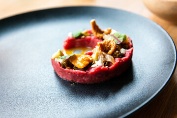 Fresh traditional polish beef tartar served with mushrooms, mustard and fresh lettuce on black ceramic plate ready to be served