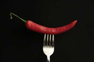 red pepper in a fork on a black background