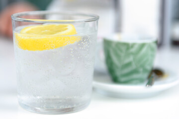 Glass of sparkling water with lemon and cup of coffee. Iced mineral water with lemon and cup of coffee on the white table.