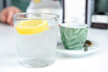 Glass of sparkling water with lemon and cup of coffee. Iced mineral water with lemon and cup of coffee on the white table.