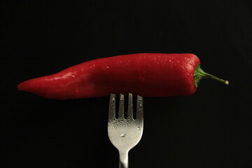 red pepper in a fork on a black background