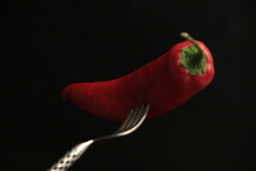 red pepper in a fork on a black background
