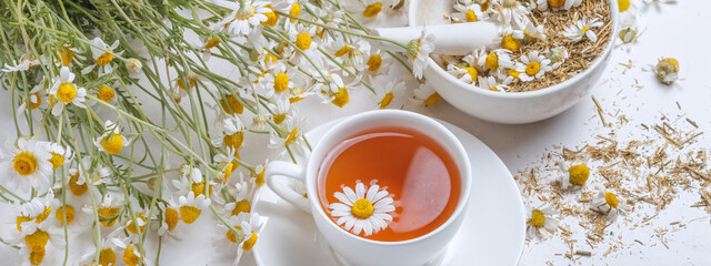 Rural still-life - cup of brewed chamomile tea on the background of a bouquet of daisies, closeup