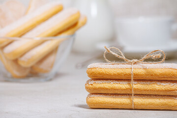 Traditional italian savoiardi or ladyfingers cookies in a stack, tied with a rope. Biscuits on a plate, a white cup and a jug of milk in the background. Selective focus.