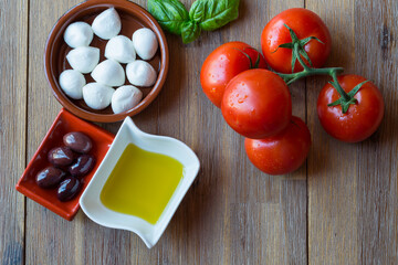 close up of tomatoes, fresh mozzarella, olives and olive oil on a wooden background