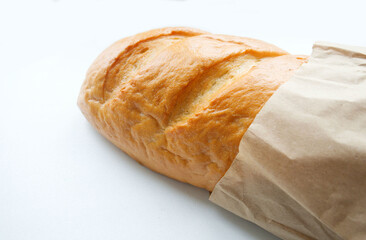 A loaf of fresh white bread, with a crust, in paper, craft packaging, on a light background. The texture of the bread, pastries, cooking, breakfast. Organic bread, paper bag.