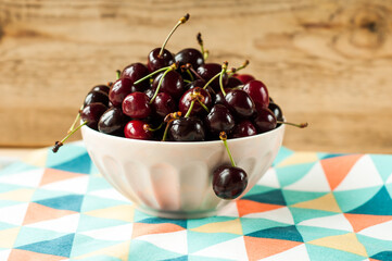 Juicy, ripe, beautiful sweet cherry on a ceramic black plate on a wooden background.