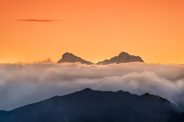 cime al tramonto 02 - due speroni di roccia innevato emergono dalla coltre di nubi al tramonto.