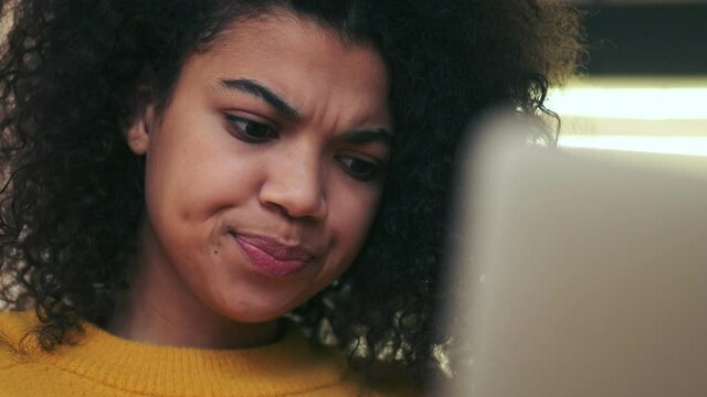 Close up view of Displeased african attractive woman using laptop computer while sitting on chair indoors