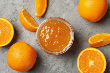 Oranges and glass jar with jam on gray background, top view