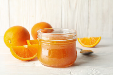 Oranges, spoon and glass jar with jam on white wooden background