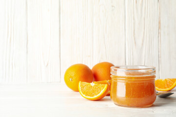 Oranges, spoon and glass jar with jam on white wooden background