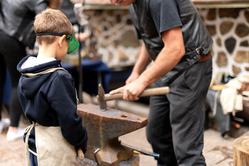 small boy in protective glasses watches the work of a blacksmith