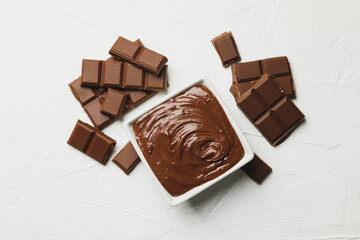 Bowl with chocolate and chocolate pieces on white background