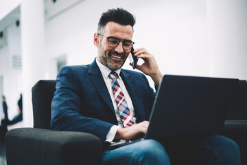 Successful mature director of financial company talking on smartphone working at modern netbook...