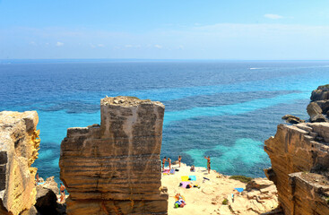the rock cliff in front of paradise clear torquoise blue water with boats and cloudy blue sky in background in Favignana island, Cala Bue Marino Beach, Sicily South Italy.