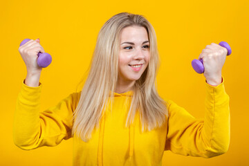 Cheerful beautiful young blonde woman in casual yellow sporty clothes doing exercises with small...